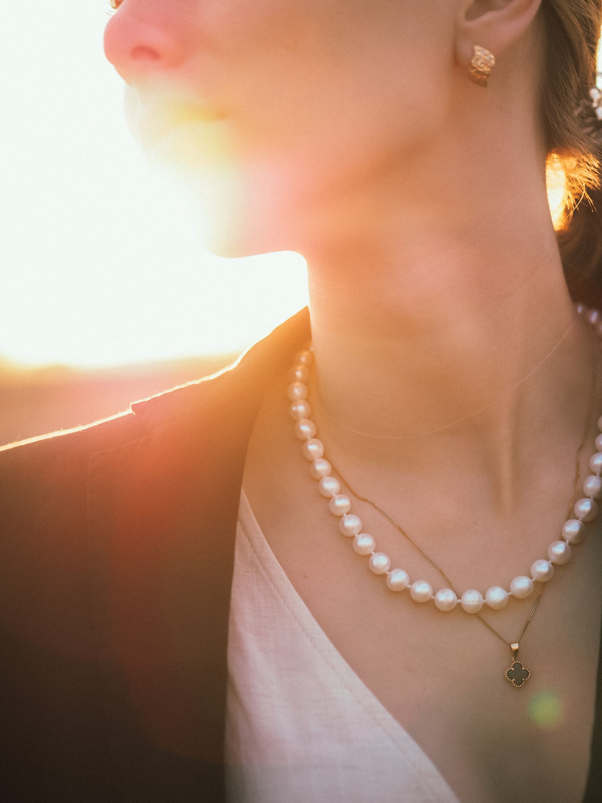 A woman wearing layered pearl necklaces, lit by golden hour sunlight
